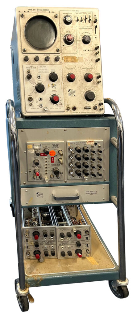 Vintage electronic test equipment with multiple dials and connectors on a wheeled cart.