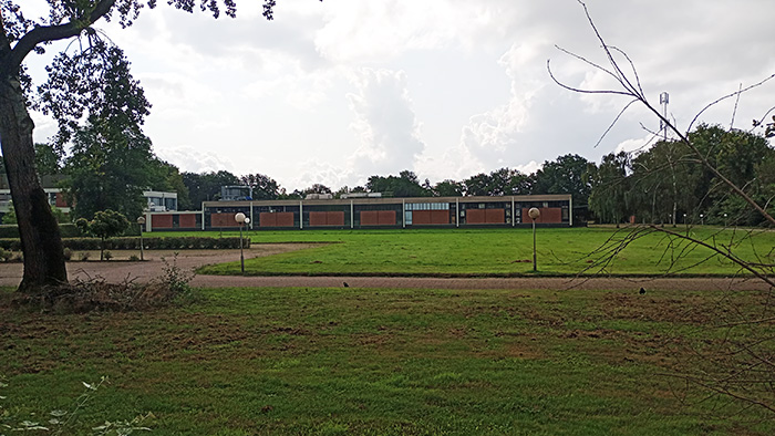 A sports field with a long building and trees in the background.